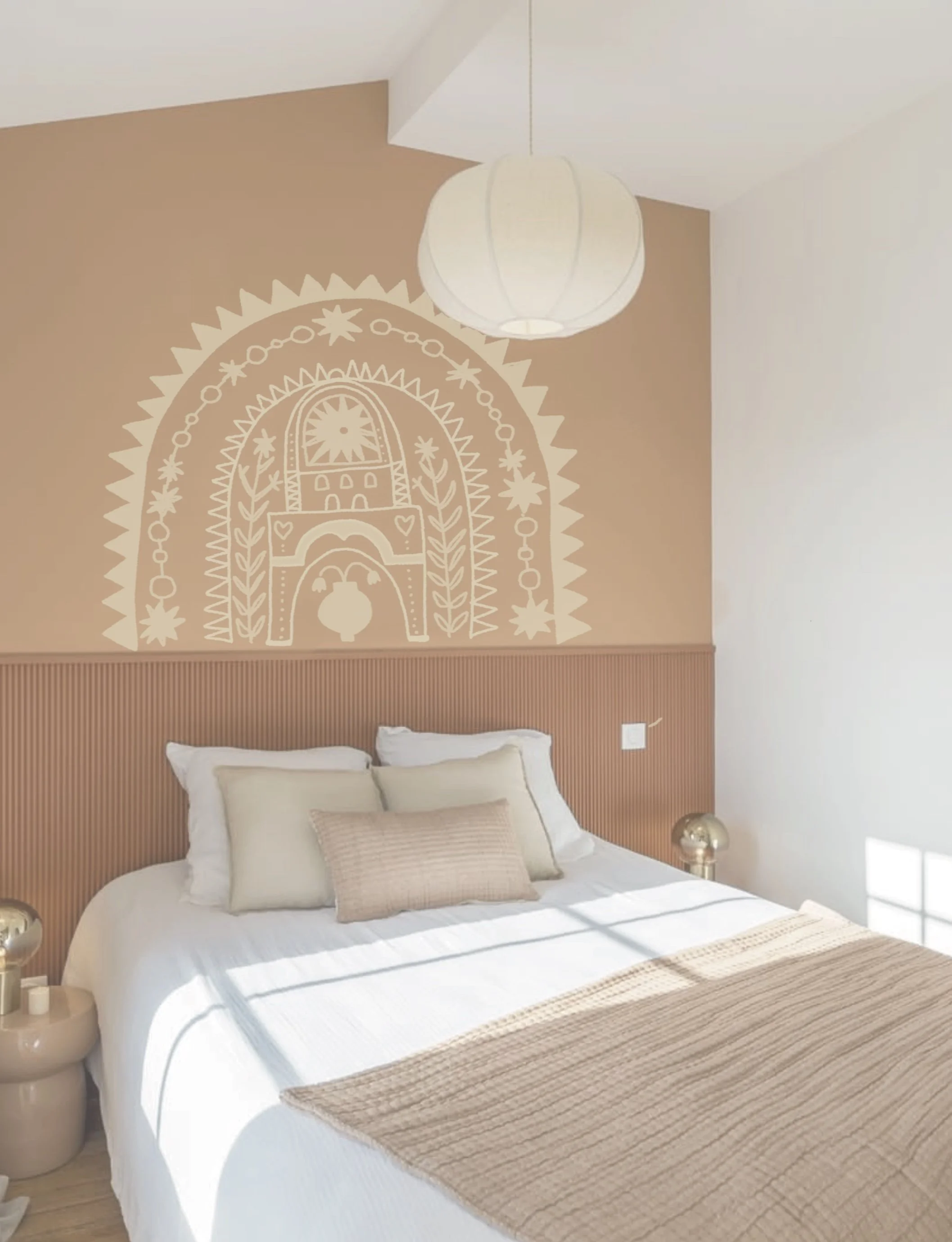 A cozy bedroom with a white bed, beige and light-colored pillows, a beige blanket, and a wooden headboard. The wall above the bed has a decorative, abstract mural in a cream color, and there is a white paper lantern ceiling light. Sunlight is streami