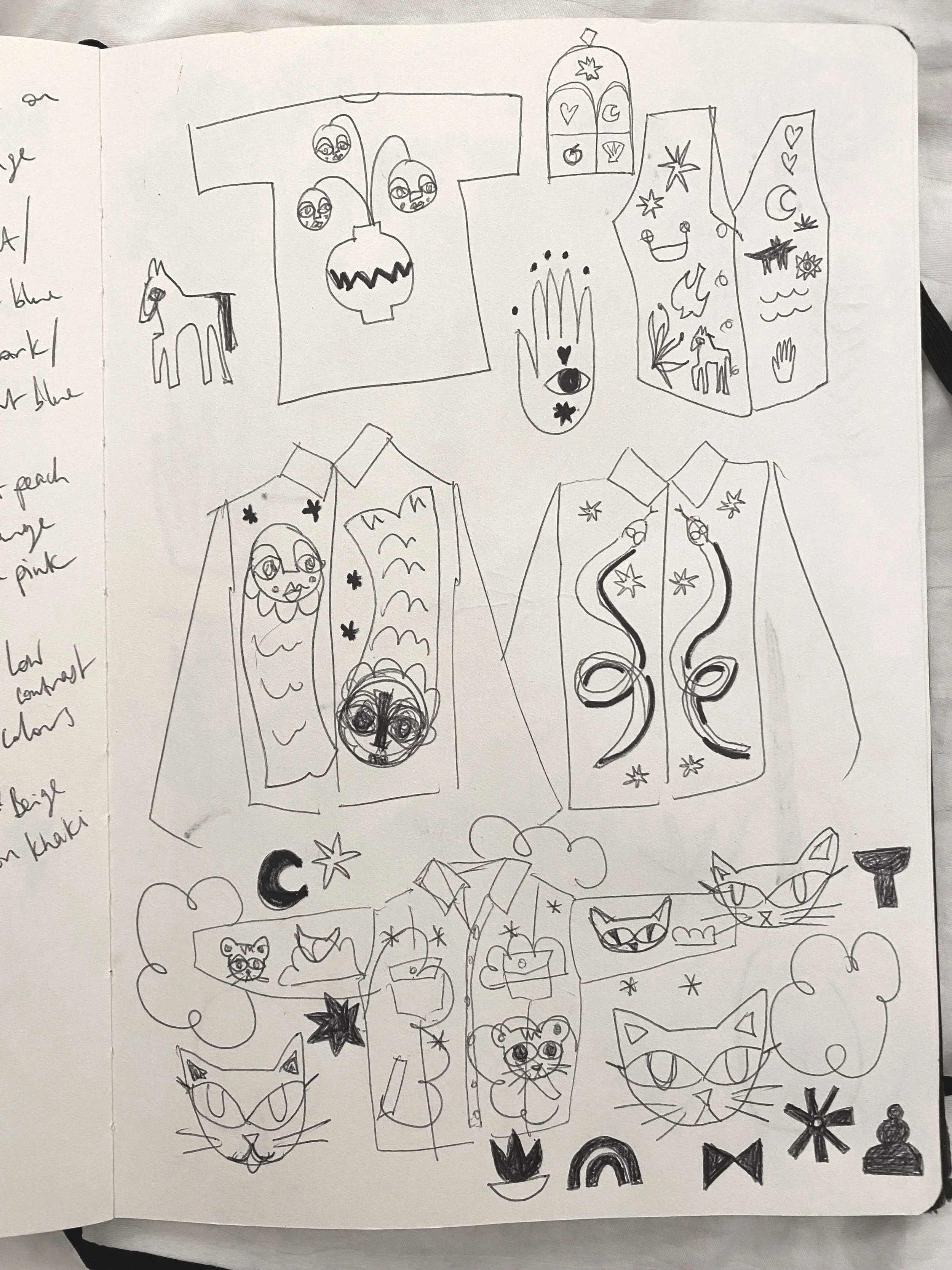 A sketchbook page filled with various doodles, including a T-shirt design, a shirt with star patterns, a shirt with swirling designs, two cats’ faces, a tree, a horse, a moon and star, small symbols like hearts, flowers, and abstract shapes.