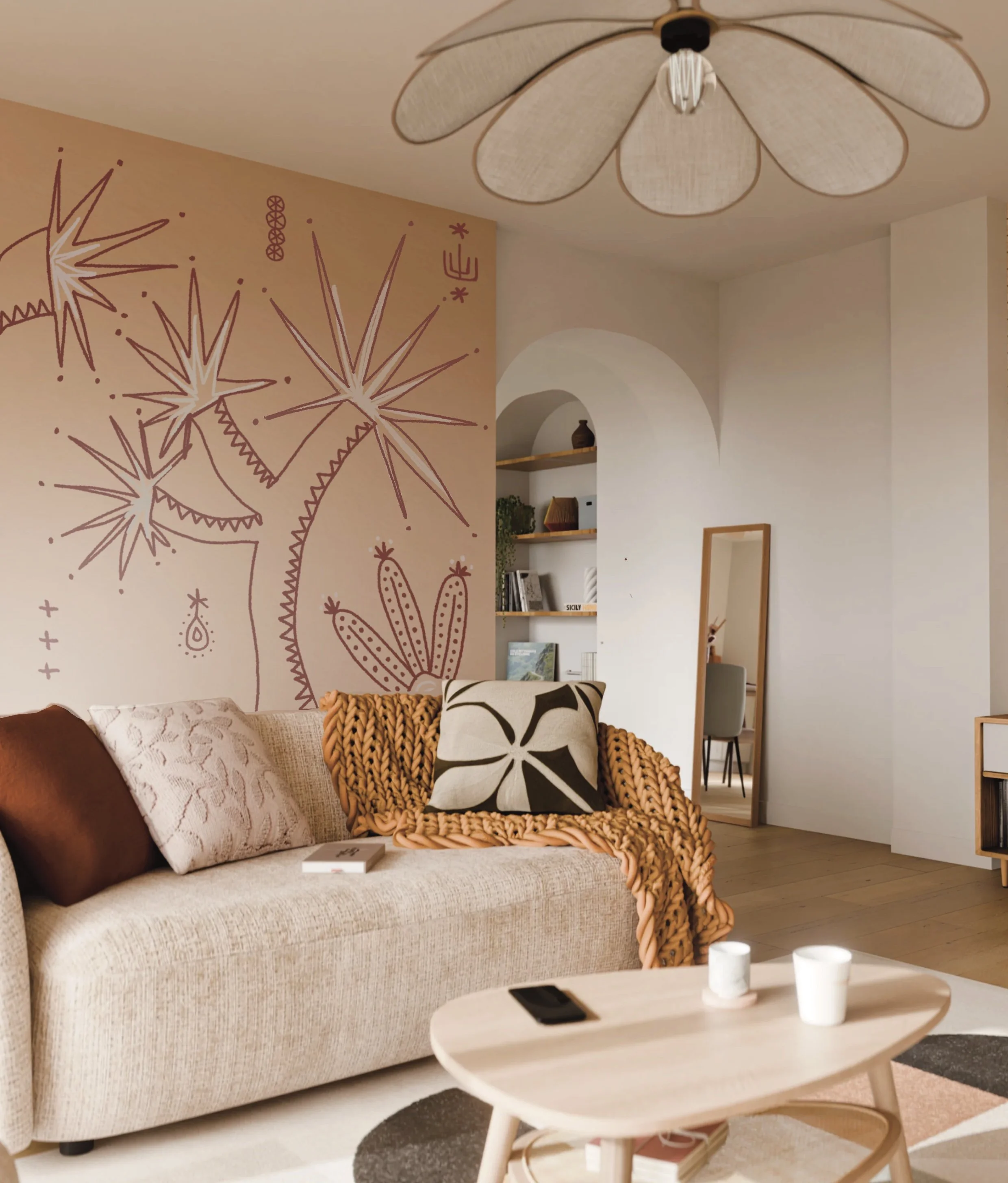 Living room with beige sofa, decorative pillows, orange chunky knit blanket, wall mural with pink/white abstract cactus and starburst designs, wooden coffee table with cups and phone, full-length mirror, bookshelf with books and plants, ceiling light