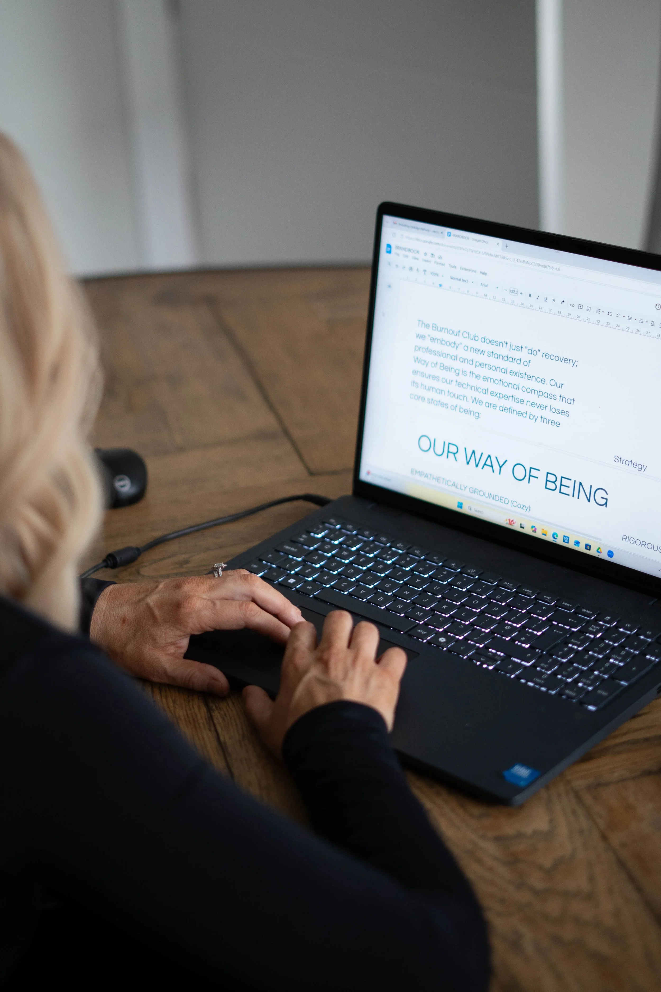 A woman typing on a laptop with an open document titled 'Our Way of Being'.
