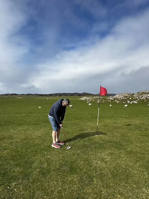 Person preparing to hit a golf ball on a green field near a red flag.