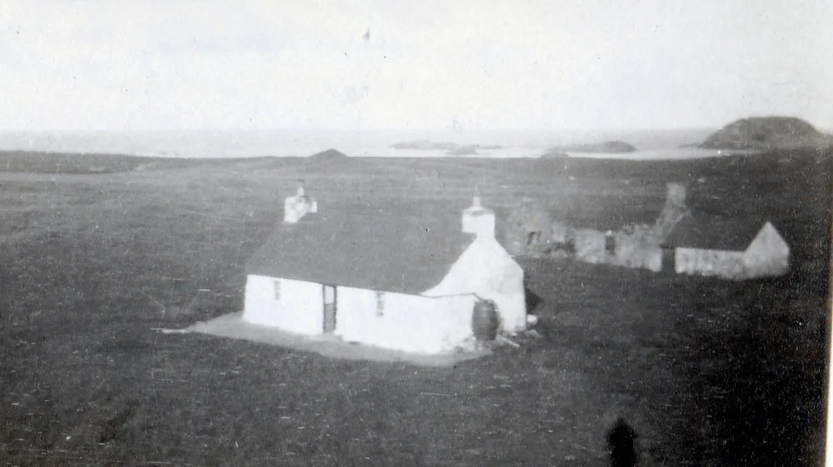 Black and white photo of a small stone church in a rural landscape with hills in the background