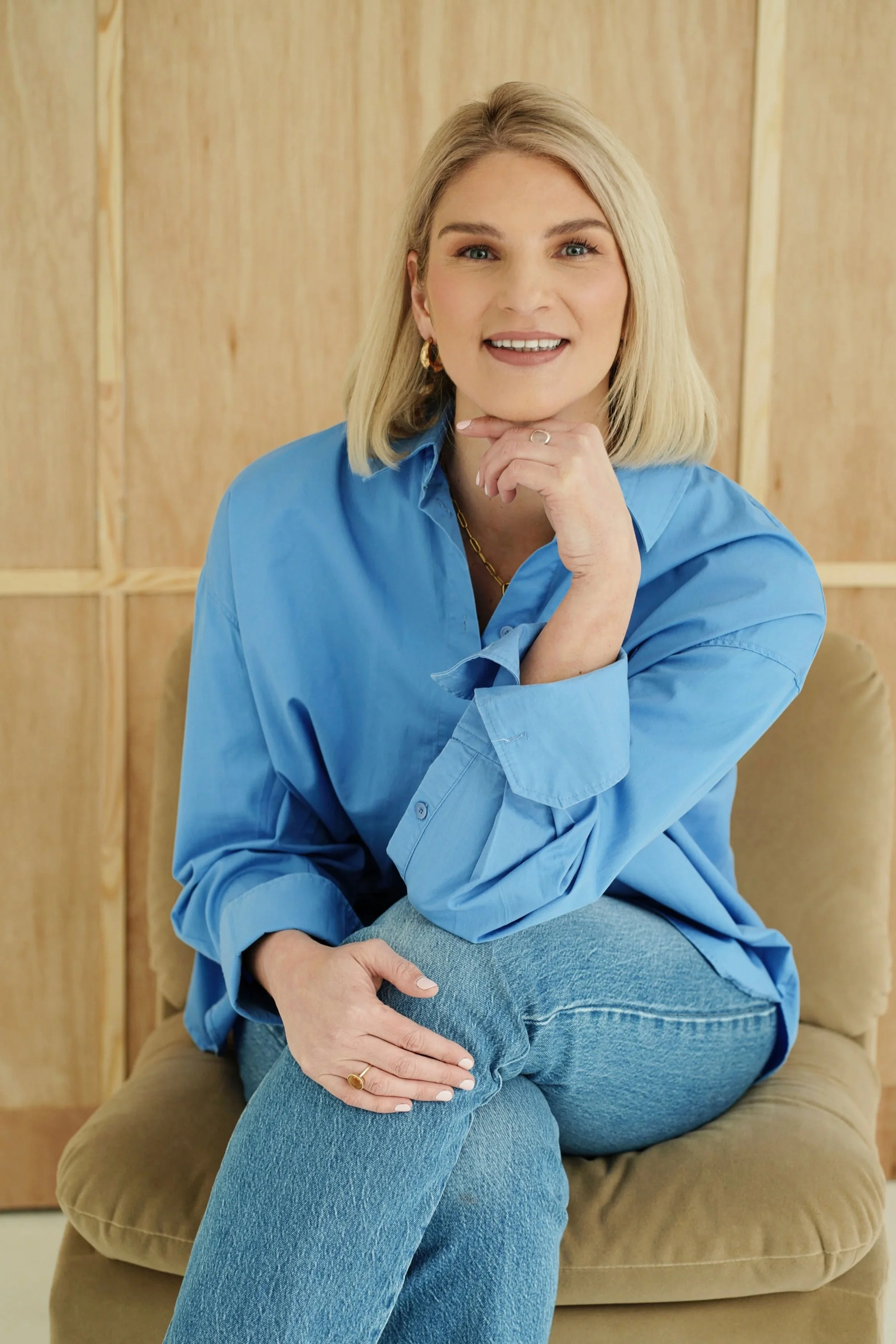 Sarah E Mold Leadership coach sat in blue shirt smiling, legs crossed on beige chair