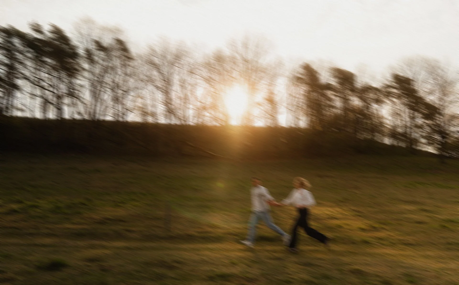 Zwei Kinder spielen im Park bei Sonnenuntergang, im Hintergrund Bäume, leicht verschwommen.