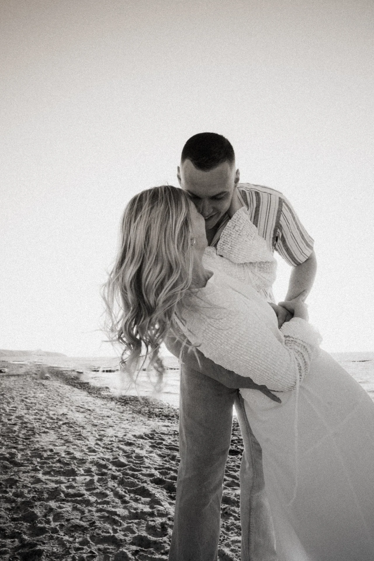Ein Paar am Strand, das sich umarmt und liebevoll ansieht, bei Sonnenuntergang oder Sonnenaufgang, schwarz-weiß Aufnahme.