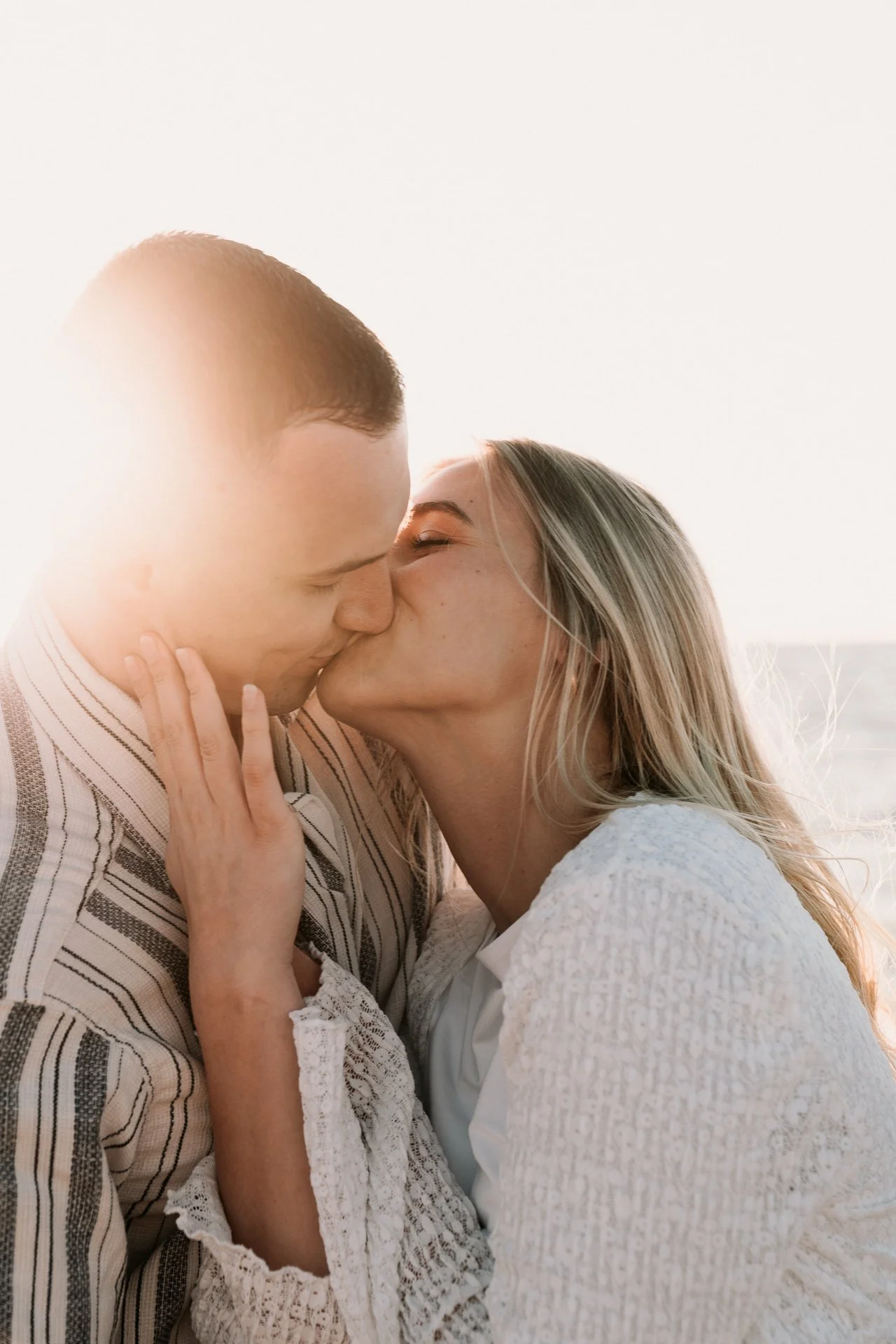 Ein junges Paar küsst sich liebevoll, die Frau hält den Kopf des Mannes sanft in der Hand, im Hintergrund ist ein hell erleuchteter Himmel.