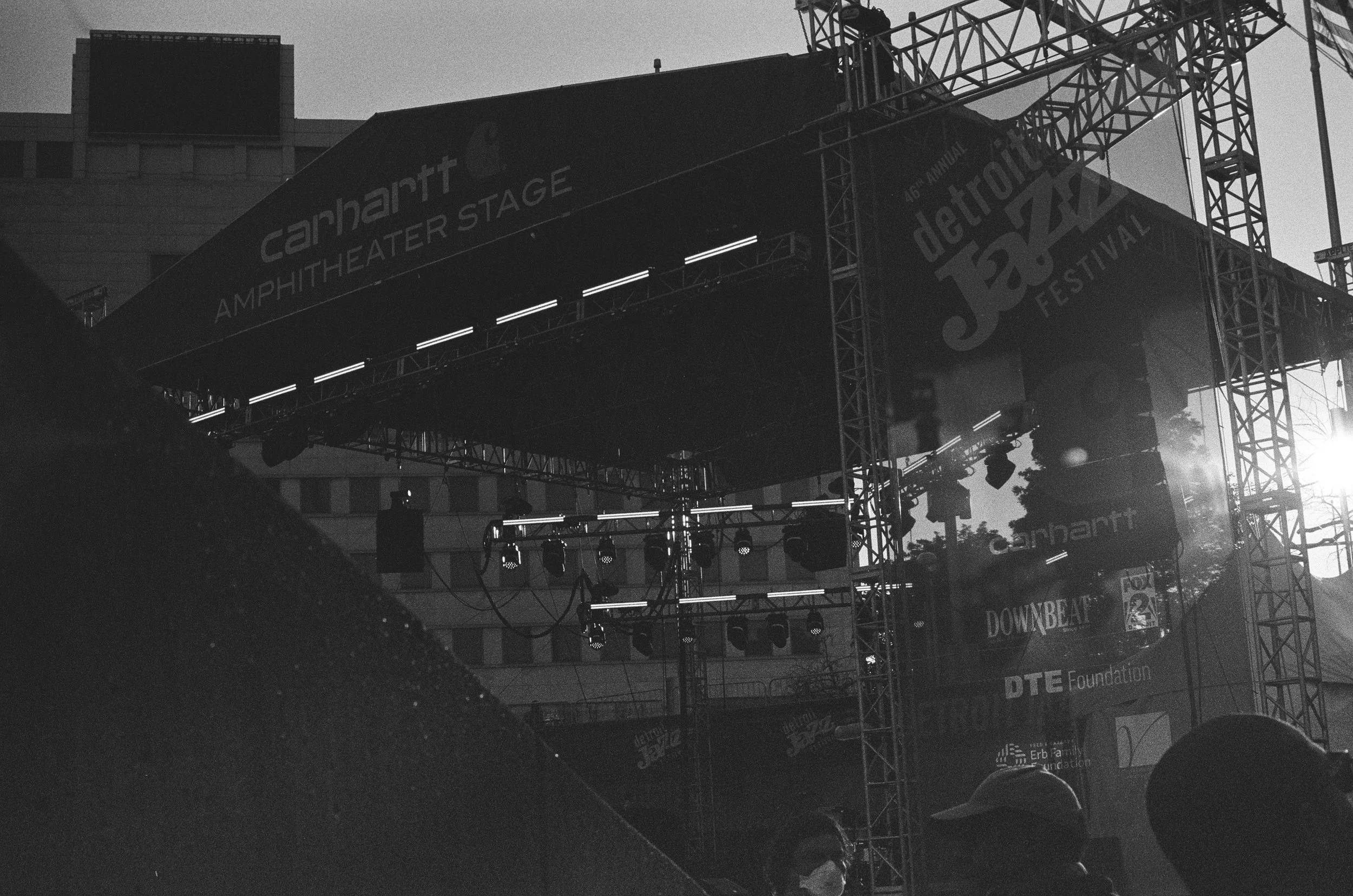 Empty stage with lights and rigging at the Detroit Jazz Festival, with some people in the foreground.