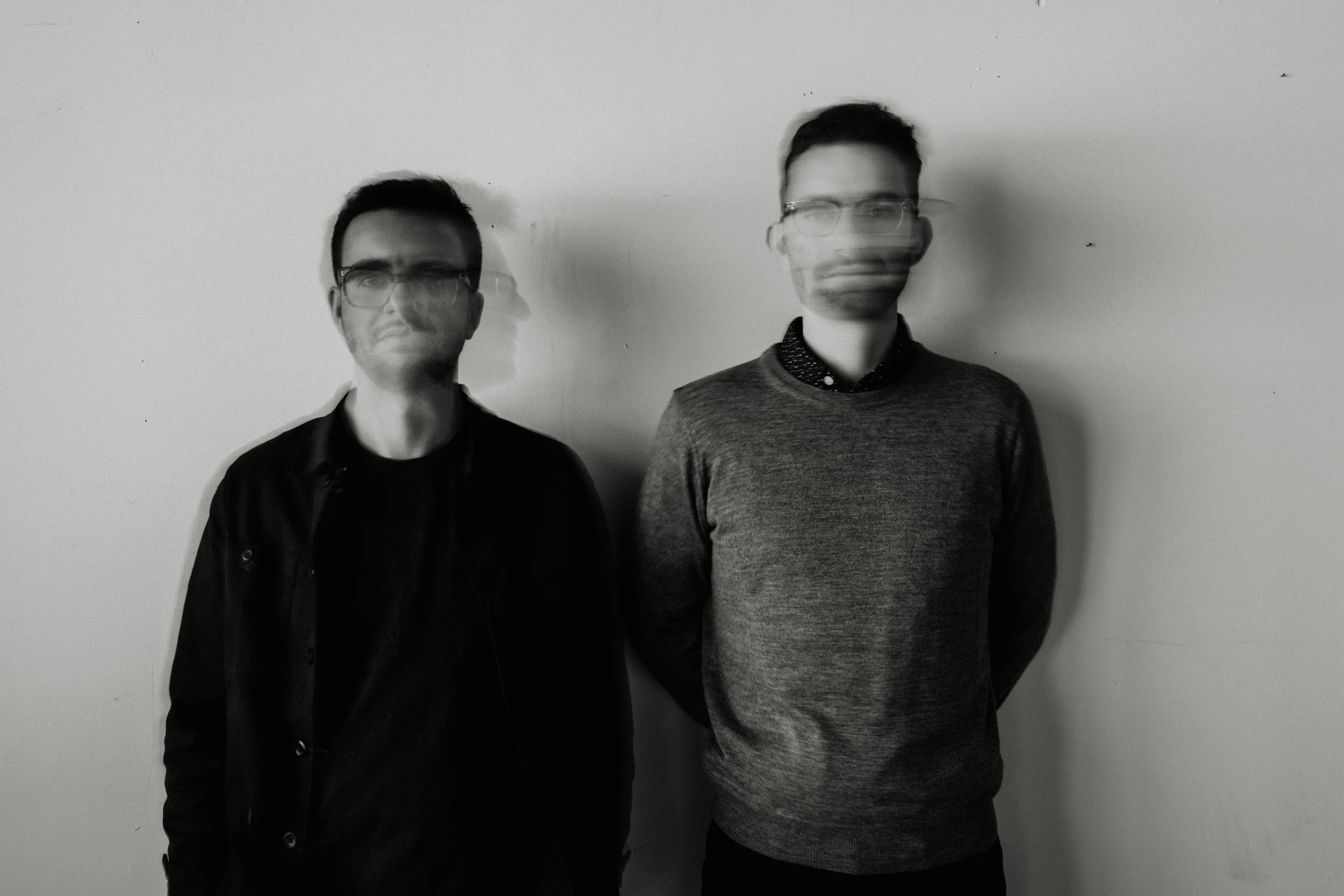 Black and white photo of two young men standing against a plain wall; the image appears blurry and distorted.