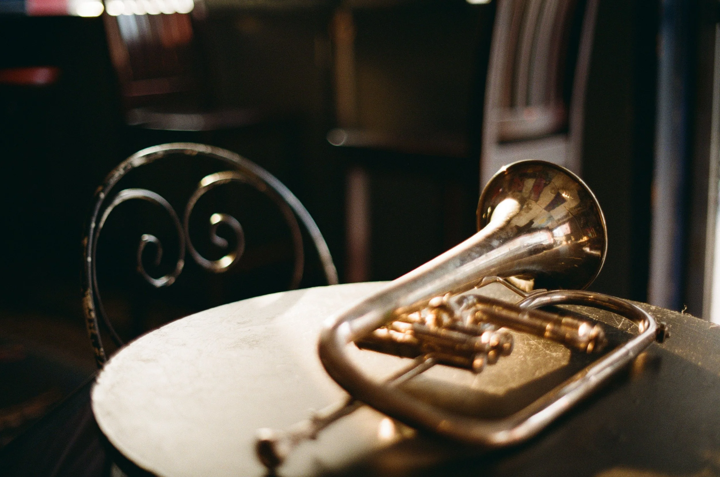 A silver flugelhorn resting on a black surface in front of a decorative metal chair.