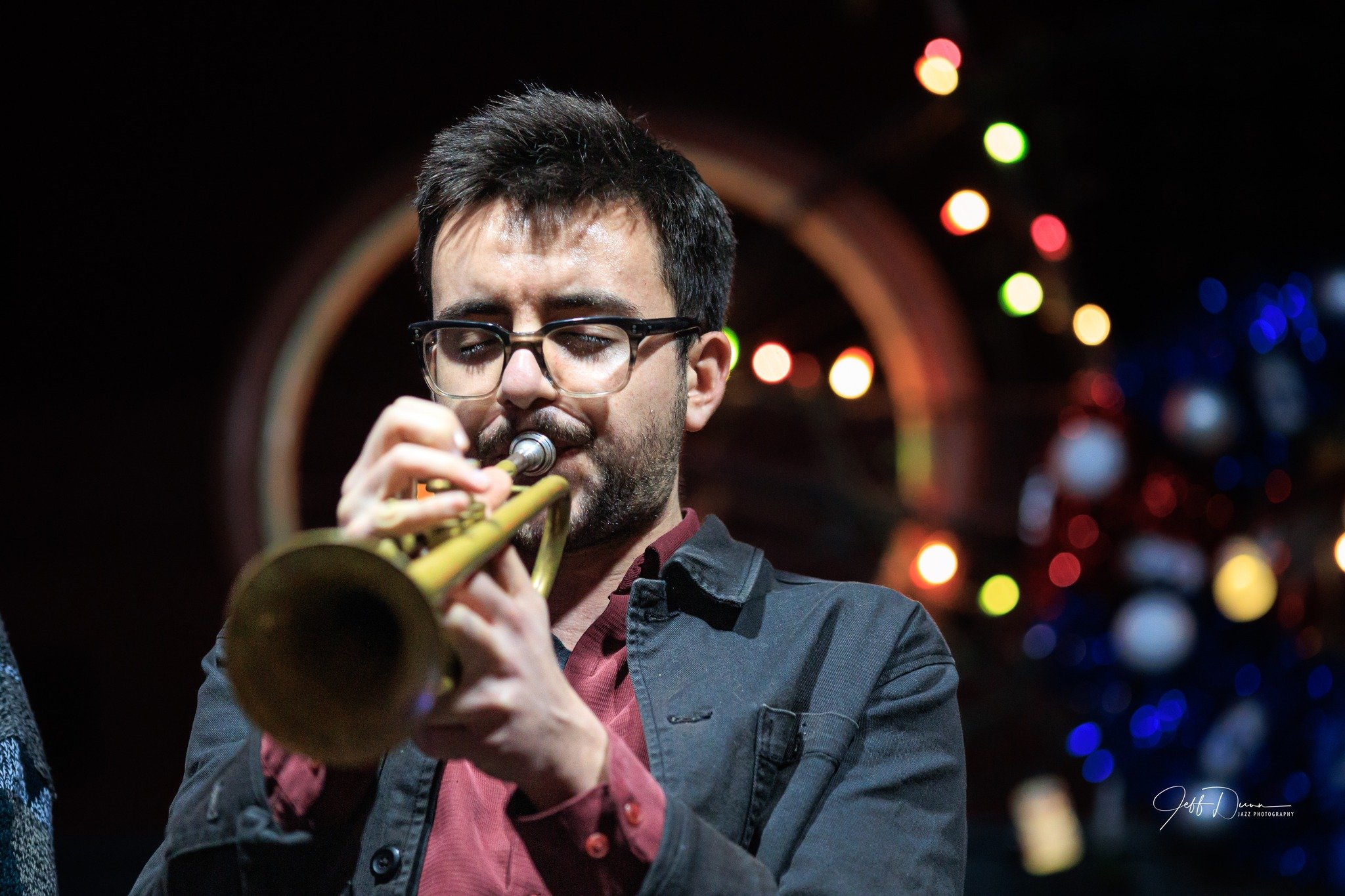 Austin Di Pietro playing a trumpet at a jazz performance, with colorful blurred lights in the background.
