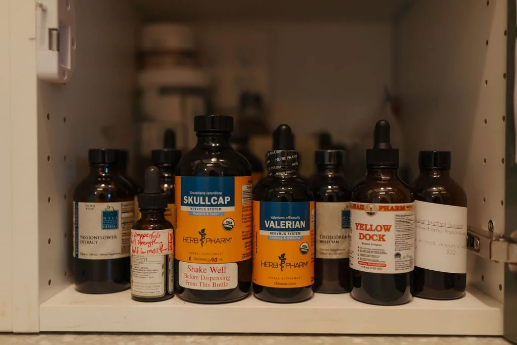 Collection of herbal supplement bottles on a cabinet shelf, including Skullcap, Valerian, Passionflower, and Yellow Dock.
