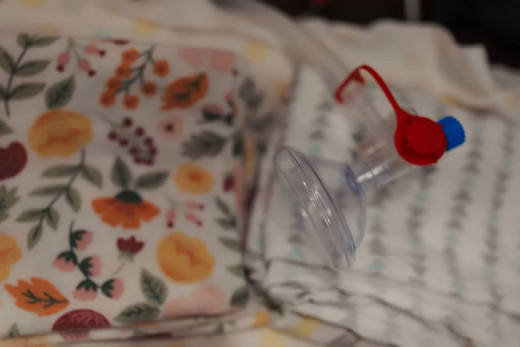 A close-up of a flower-patterned box, a clear plastic device with a red and blue component, and a white and gray striped cloth in the background.