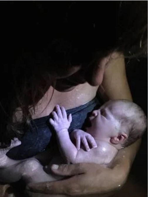 A woman breastfeeding a newborn baby in a dark setting.