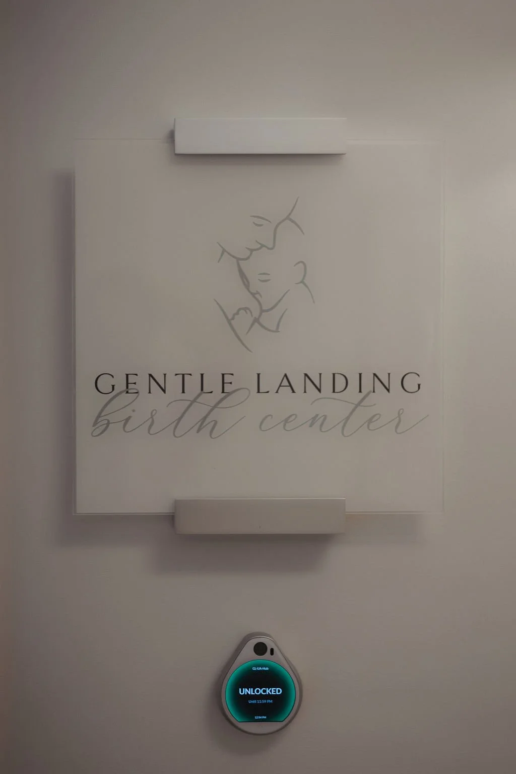 Sign for Gentle Landing Birth Center with a line art image of an adult and baby, and a digital lock displaying 'Unlocked'.
