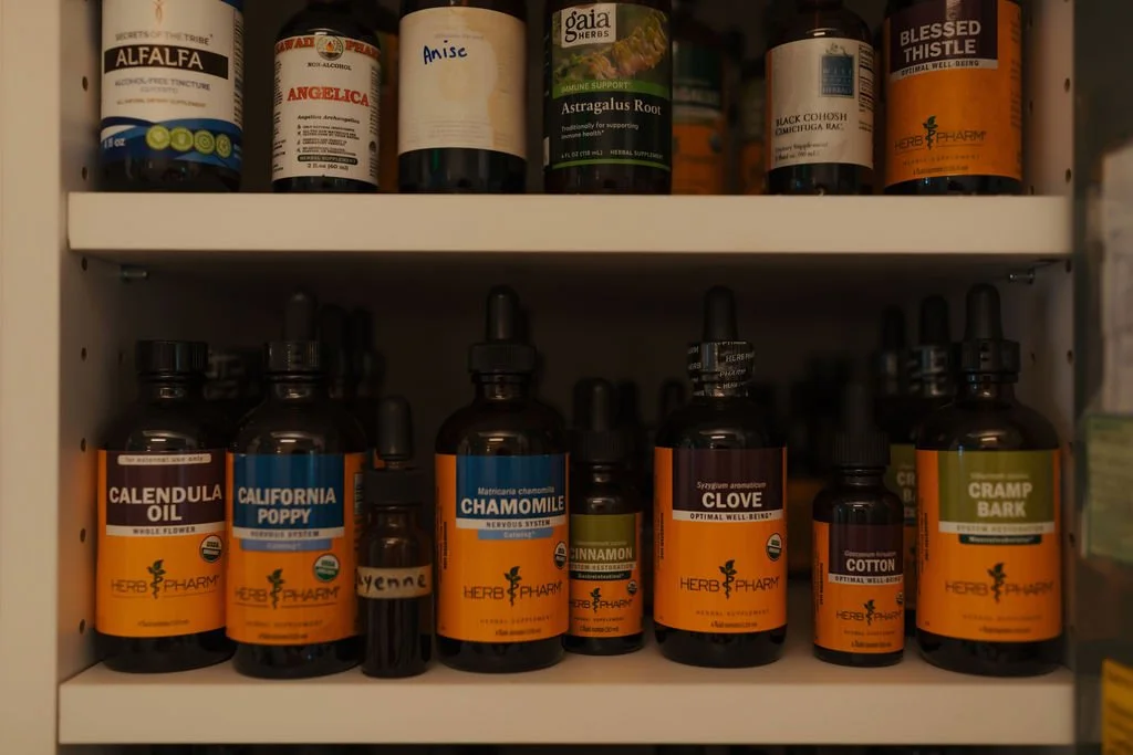 Shelf with various herbal supplement bottles including Alfalfa, Angelica, Anise, Astragalus Root, Black Cohosh, Blessed Thistle, Calundula Oil, California Poppy, Chamomile, Clove, Cotton, and Cramp Bark.