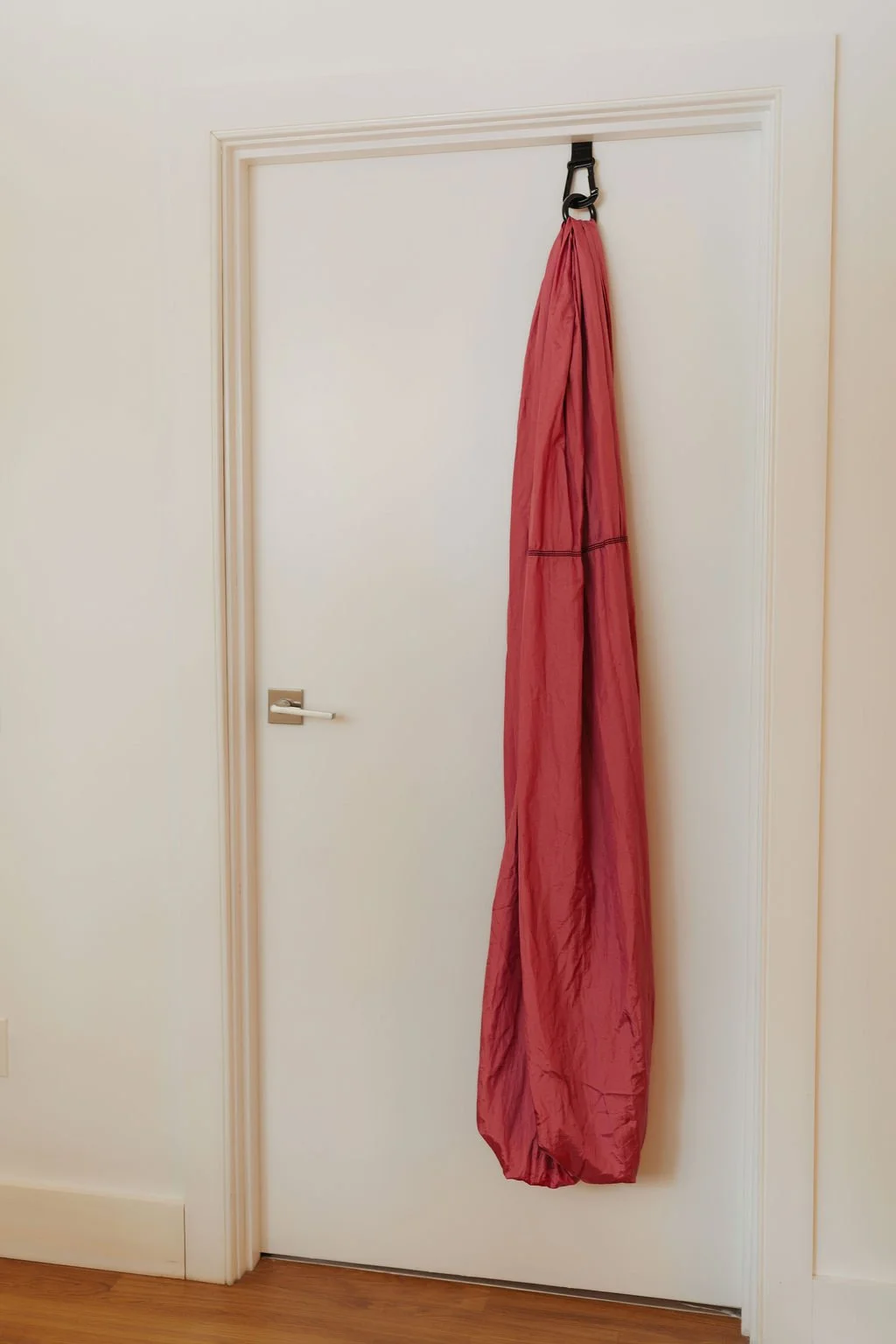 Pink fabric bag hanging from a hook on a white door.