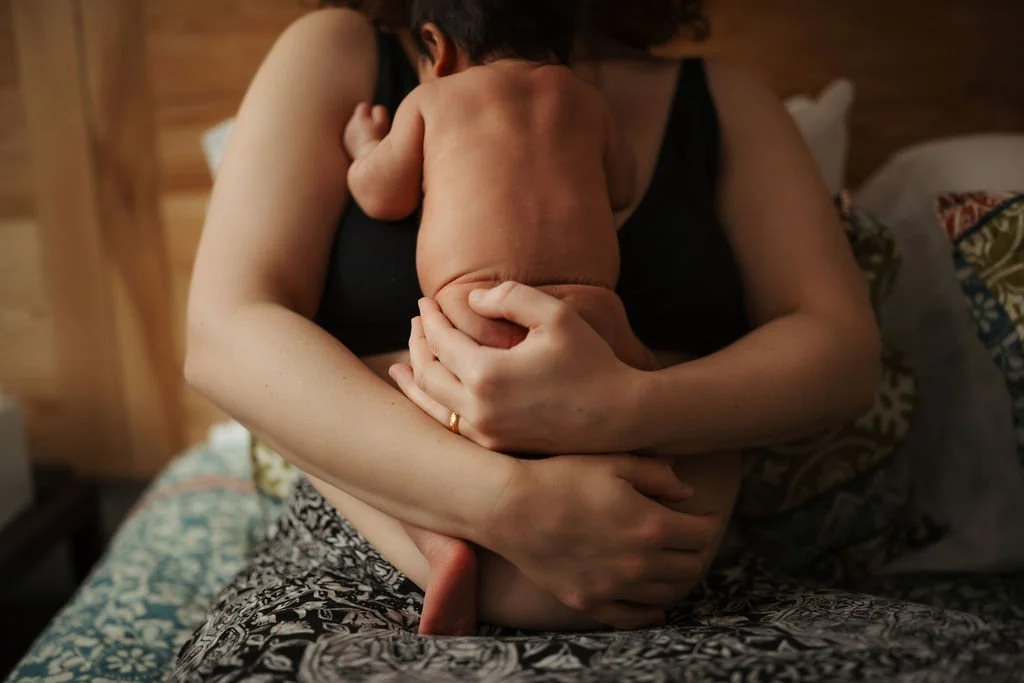 A woman holding a naked baby on her lap in a cozy bedroom.