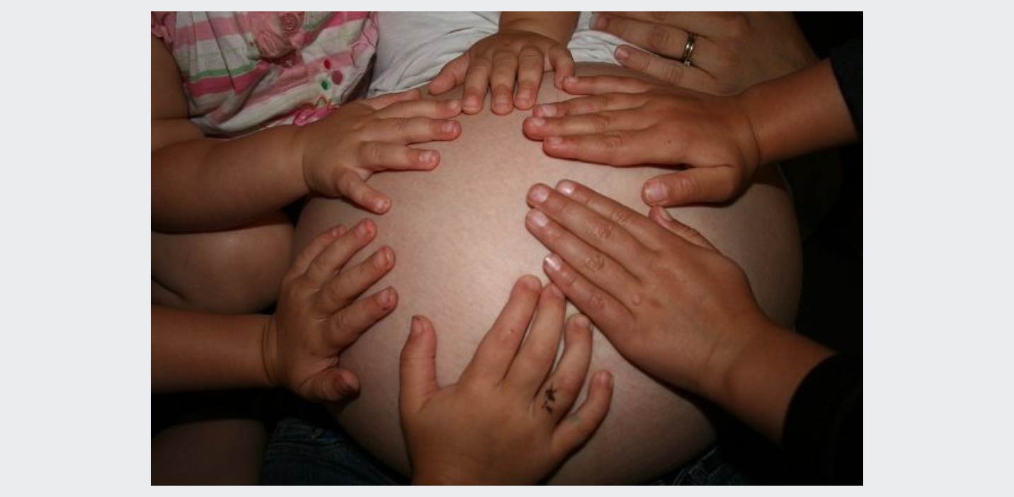 Multiple hands of different sizes and skin tones placed on a pregnant belly, suggesting a family or supportive group.
