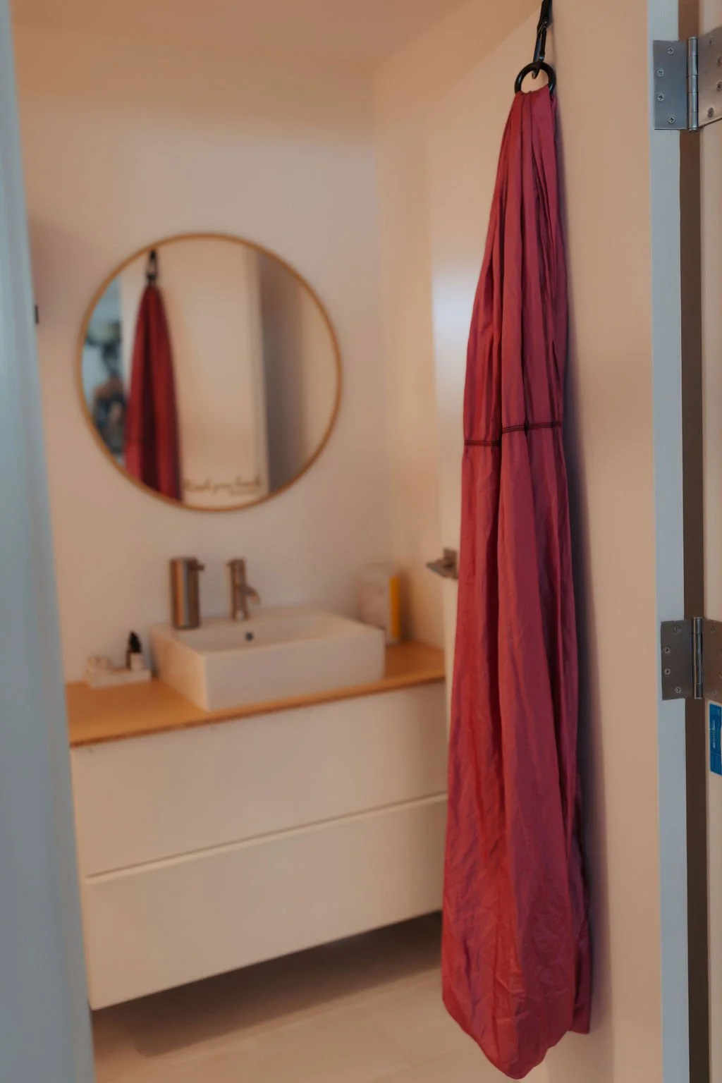 View of a bathroom vanity with a round mirror, a rectangular vessel sink, and a red shower curtain hanging on the side.