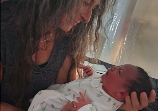 A woman with long, curly hair looking at a newborn baby who is wrapped in a blanket, lying in the woman's lap.