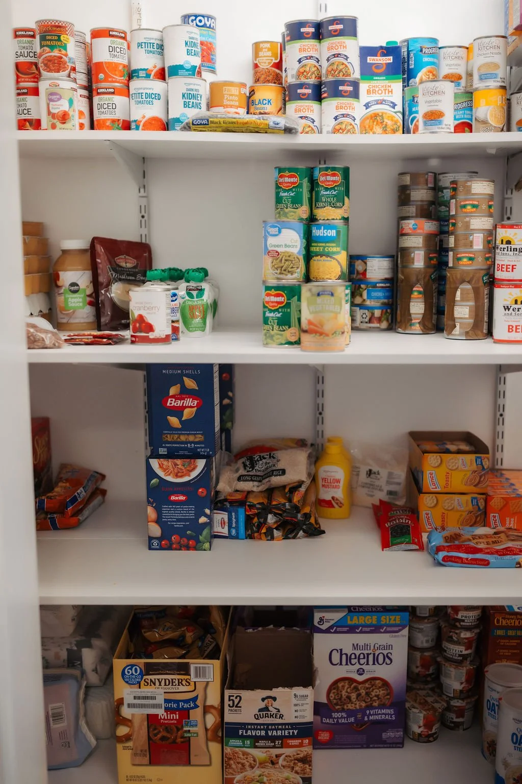 A pantry shelf filled with canned foods, boxes of pasta, cereal boxes, jars of sauces, and various snacks.