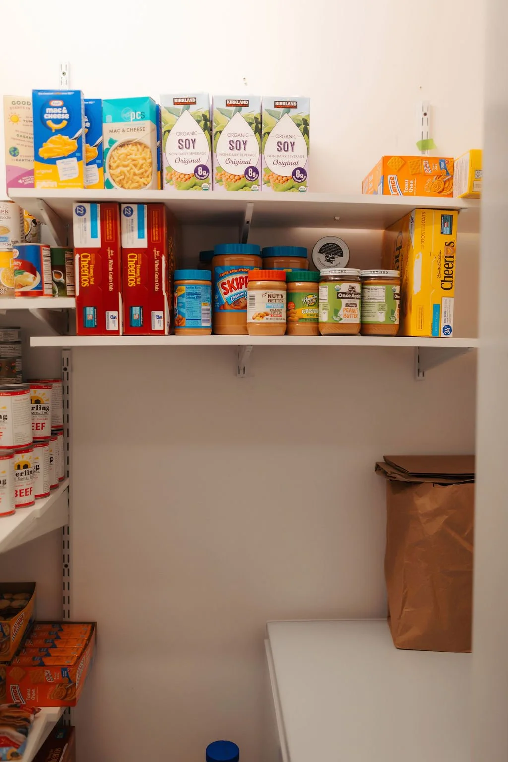 Pantry shelf with macaroni and cheese, soy milk, peanut butter, canned goods, and snack boxes.
