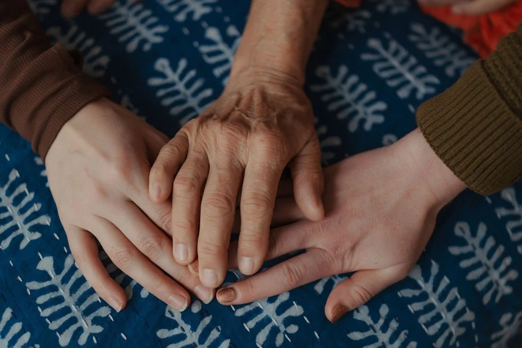 Three hands of different ages intertwined over a blue patterned blanket.