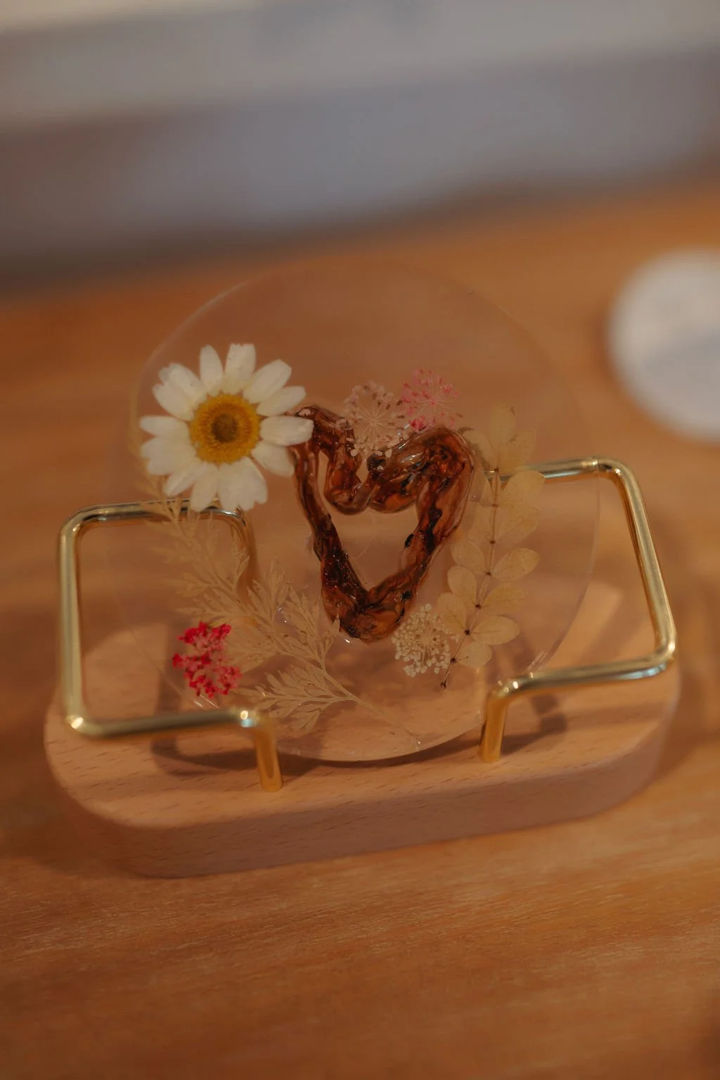 A glass decorative piece with dried flowers and a heart-shaped twig inside, placed on a wooden surface.
