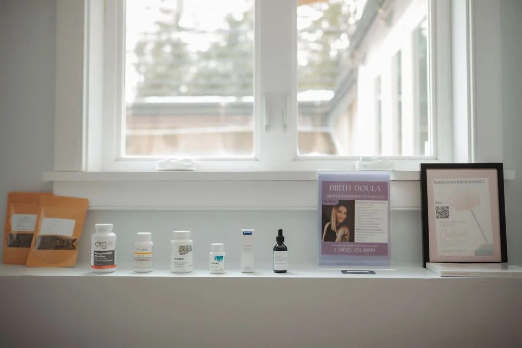 A windowsill with various bottles of supplements and medications, framed informational posters about birth doula services, and traditional herbal packets for herbal medicine.