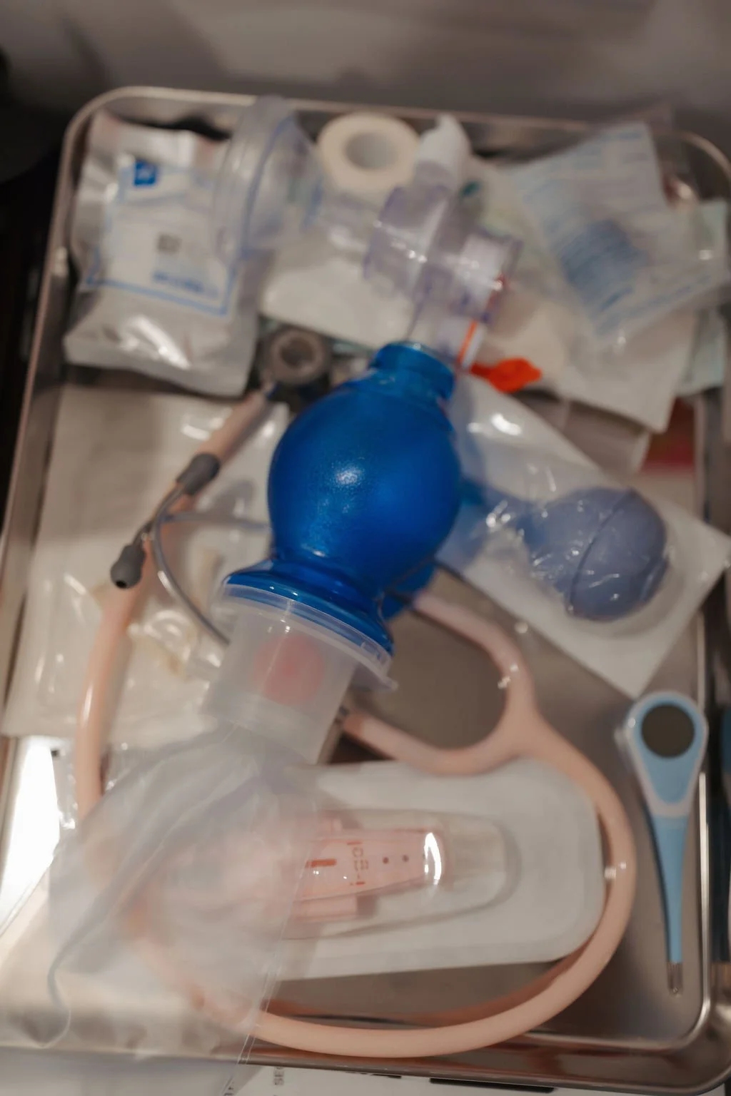 Medical supplies including a blue manual resuscitation bag, a clear mask, tubing, and various sterile packaging in a medical tray.