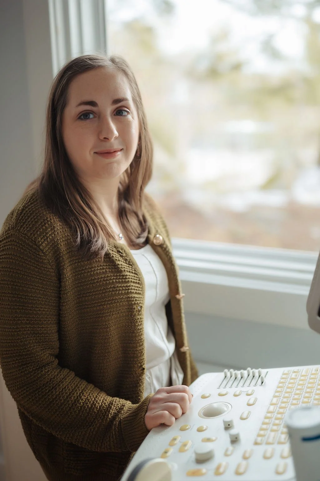 A woman standing next to an ultrasound machine by a window with an outdoor view.