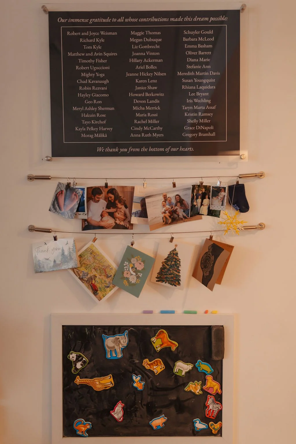A wall display featuring a framed gratitude list, a photo collage with family pictures, holiday greeting cards, and a magnetic board with colorful animal cutouts.