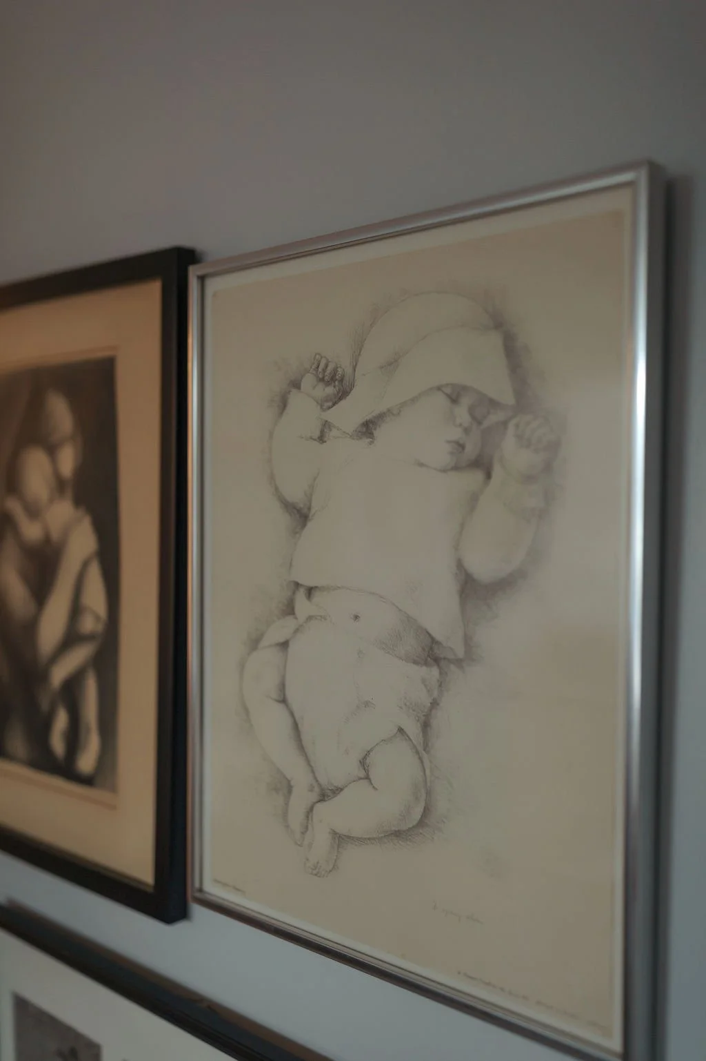 Framed pencil sketch of a child wearing a hat, with chubby arms and legs, holding their socks.