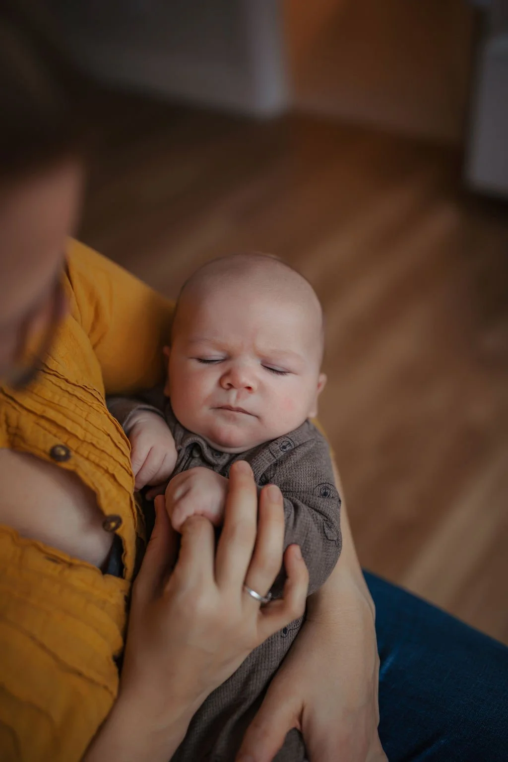A close-up of a baby being held by an adult with a yellow shirt, showing the baby's face with closed eyes and a serious expression.