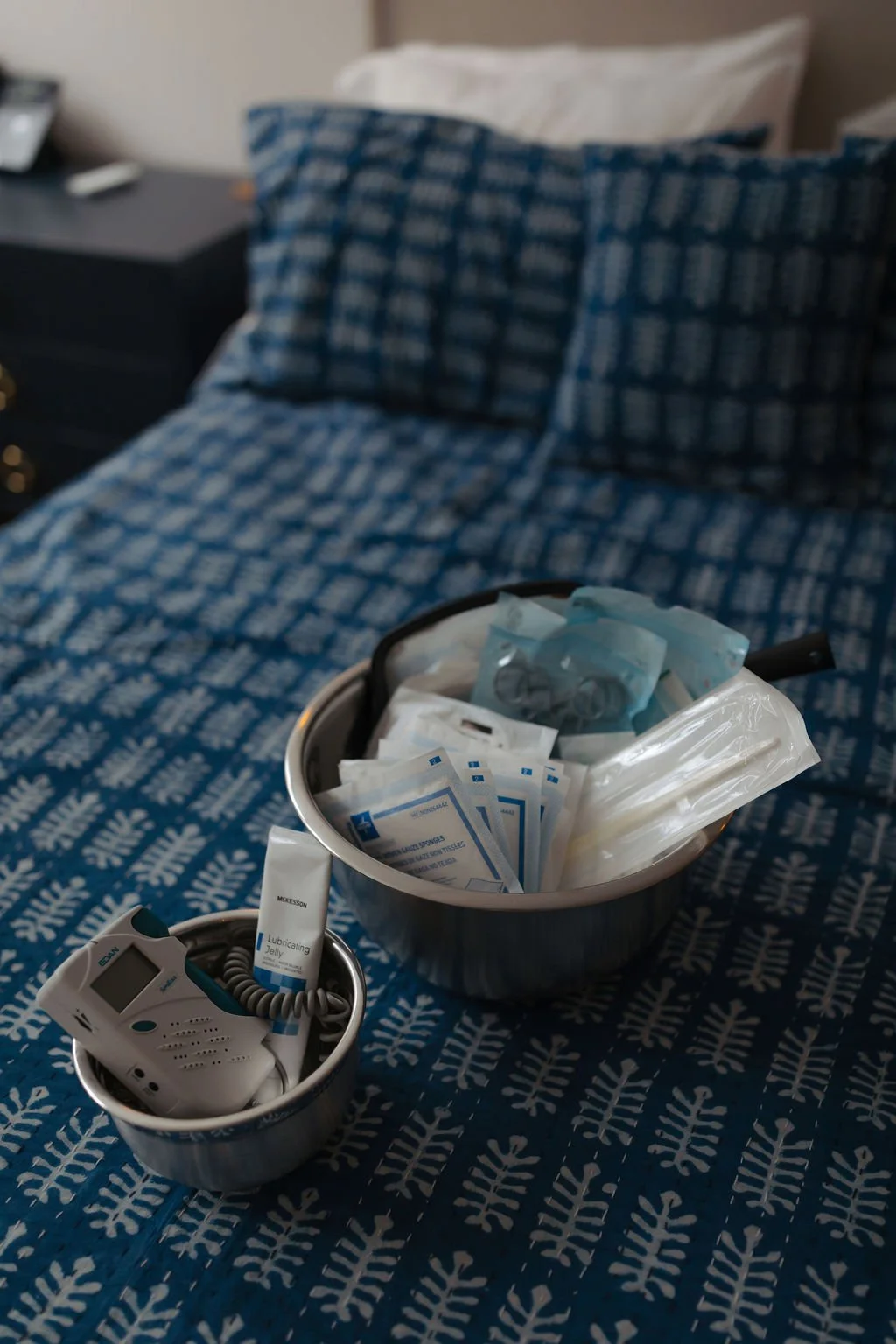 Clinic bed with medical supplies, including a blood pressure cuff, syringes, and medication, on patterned blue and white bedding.