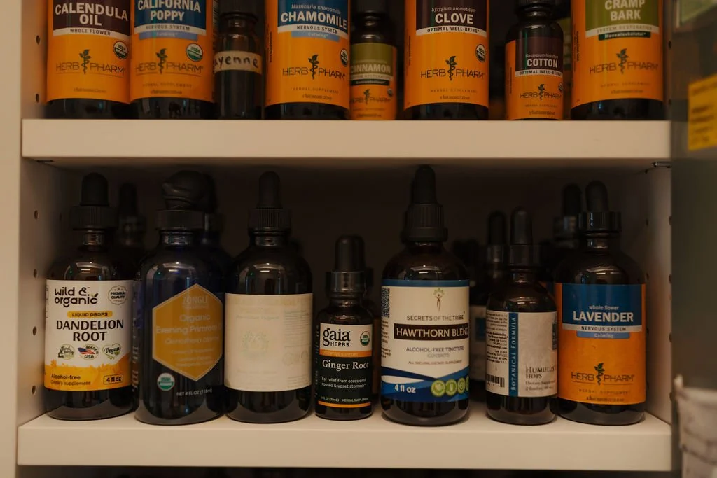A pharmacy cabinet with various herbal and natural remedy bottles, including lavender, ginger root, hawthorn blend, dandelion root, and chamomile.