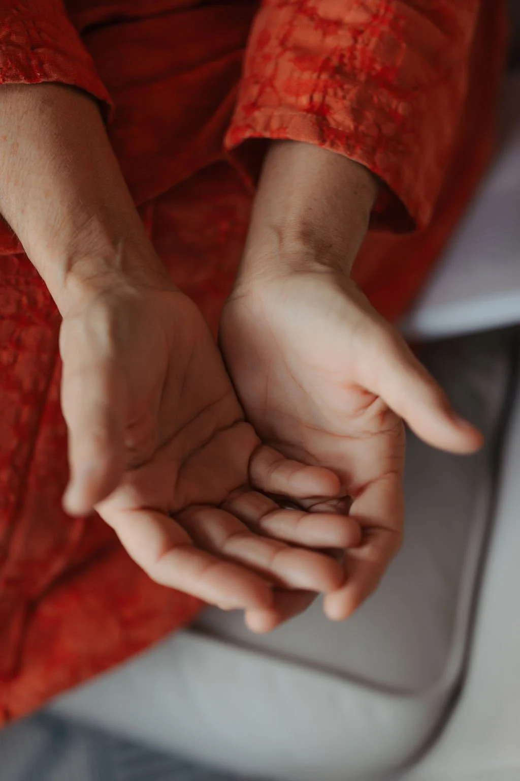 Close-up of a person's hands resting with palms facing upward, with an orange and red patterned garment visible on their arms.