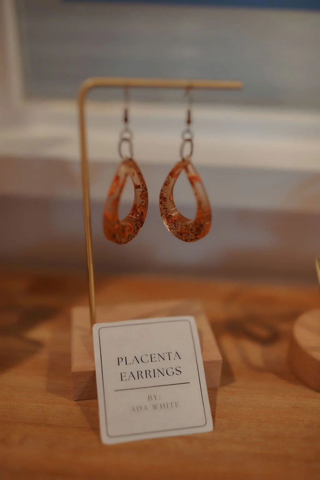 Rust-colored plandenta earrings hanging on a display stand, with a label that reads 'PLACENTA EARRINGS BY ADA WHITE'.