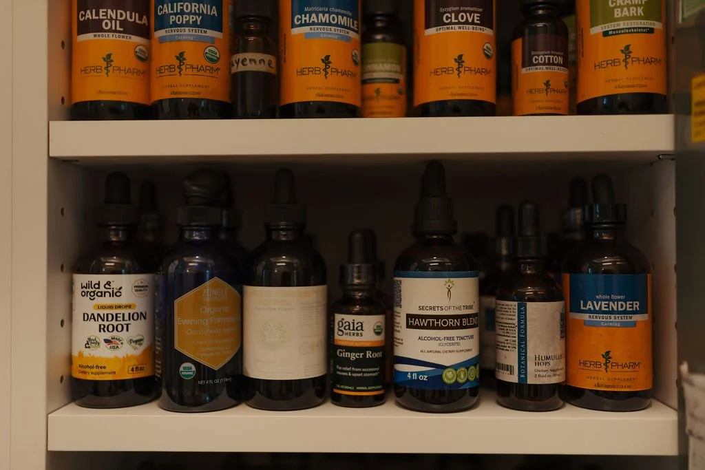 Shelf filled with herbal supplement bottles, including calendula oil, California poppy, chamomile, clove, and lavender, along with other herbal remedies and tinctures.