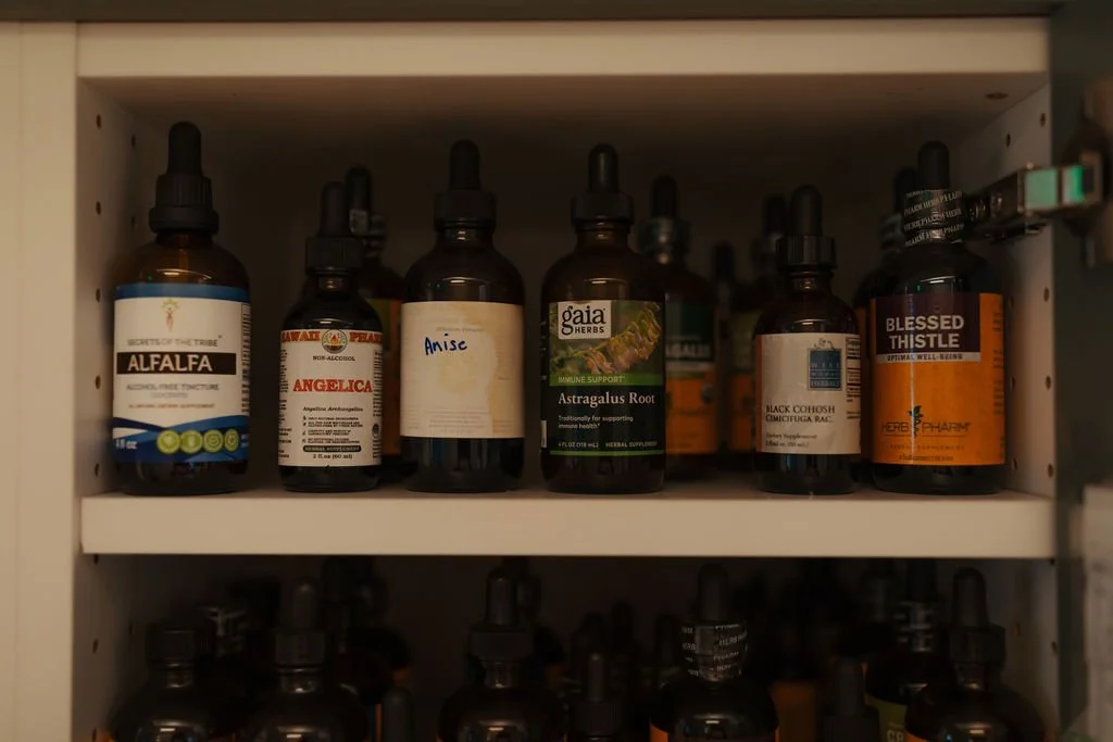 Shelf with several bottles of herbal supplements and tinctures, including Alfalfa, Angelica, Anise, Astragalus Root, Black Cohosh, and Blessed Thistle.
