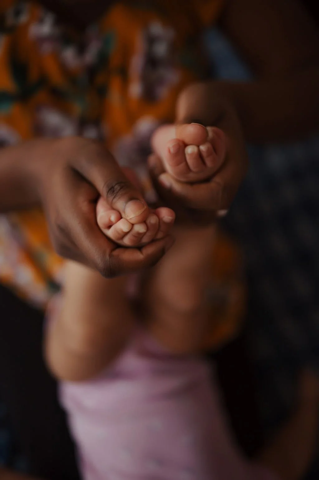 A close-up of an adult's hand holding a child's hand, both gripping each other tightly. The background is blurred, showing colorful clothing.