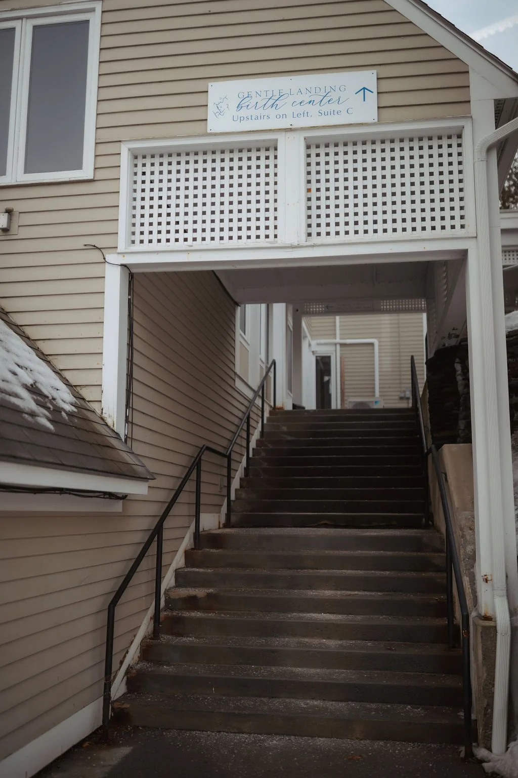 Outdoor staircase leading to the entrance of a building with a sign that reads "Gentle Landing Birth Center," with additional directions.