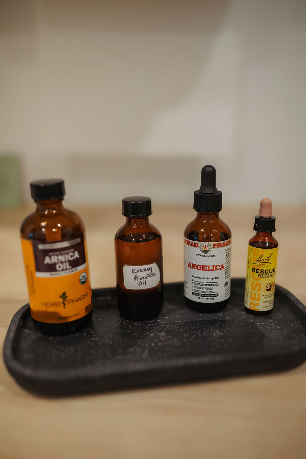 Four small bottles of herbal remedies and supplements on a black tray, including Arnica Oil, Evening Primrose Oil, Angelica extract, and Rescue Remedy.