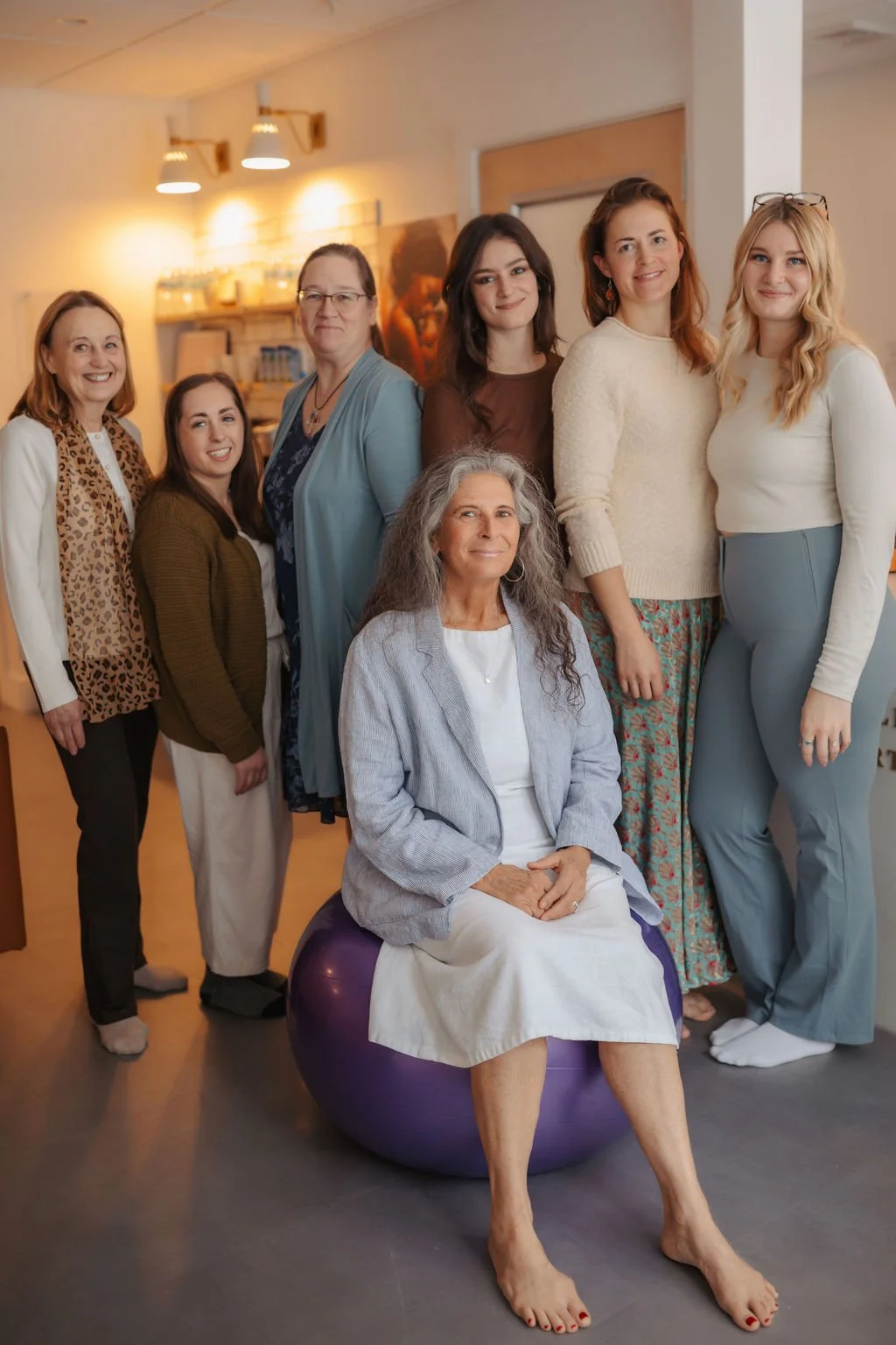 Group of women of various ages standing and sitting together indoors, smiling for the photo.