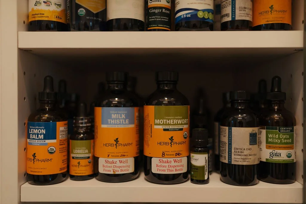 A cabinet shelf filled with herbal supplement bottles, including lemon balm, milk thistle, motherwort, and others.