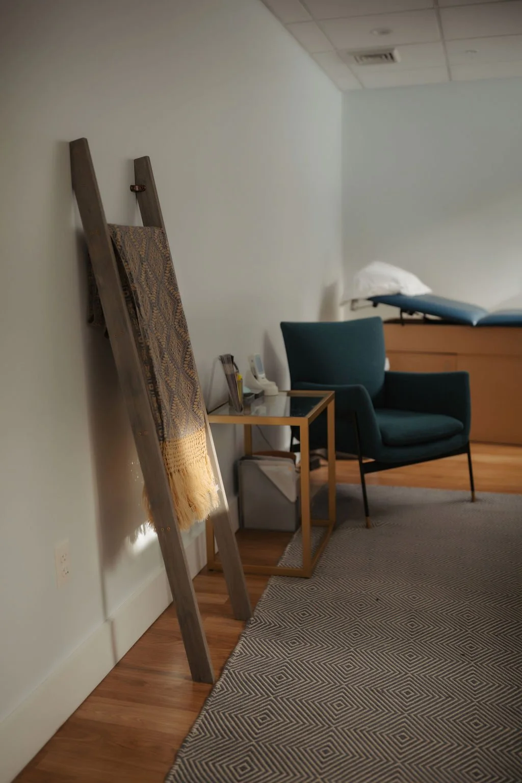 Hospital room with a bed, pillow, blue chair, small side table, climbing ladder with a throw blanket, and area rug.