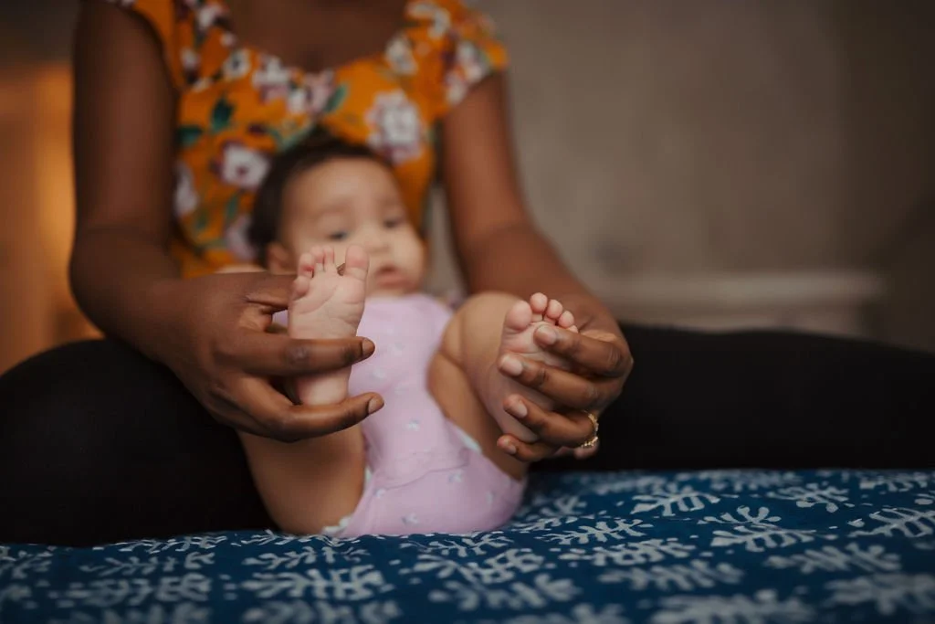 A woman helps a young child play with her feet.