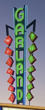 Vertical neon sign reading 'GARDLAND' with red and green diamond-shaped signs below, displaying additional text.
