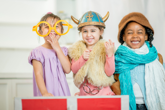 Three girls dressed in costumes, smiling and laughing in a bright room.