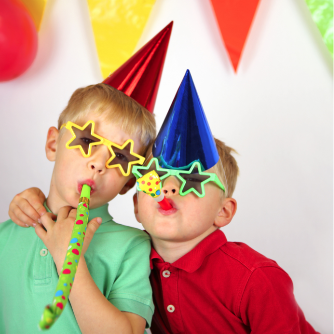 Two children wearing colorful party hats and star-shaped sunglasses at a celebration with balloons and decorations.